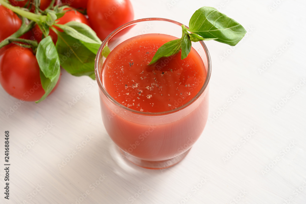fresh tomato juice in a glass with basil garnish on a white painted table, healthy smoothie drink with copy space fresh tomato juice in a glass with basil garnish on a white painted table, healthy smoothie drink with copy space
