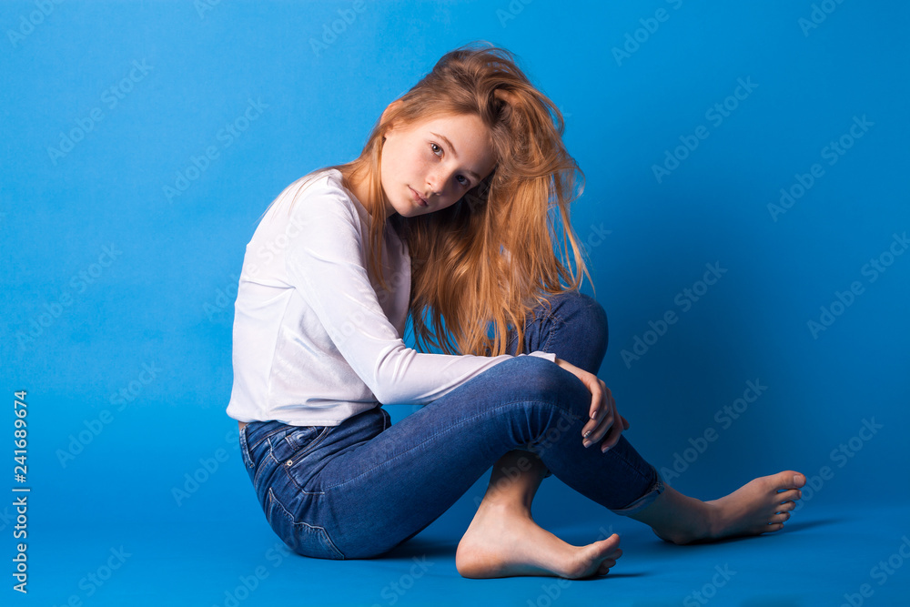 Beautiful smiling teen girl in jeans and a white blouse on blue background. Beautiful smiling teen girl in jeans and a white blouse on blue background.