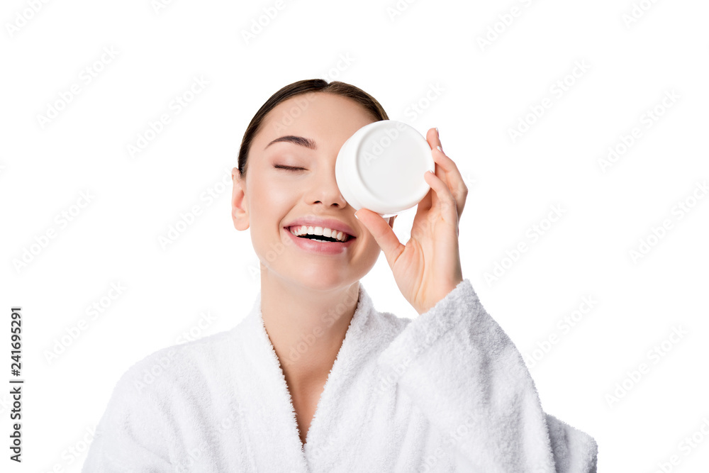 cheerful woman in bathrobe holding moisturizing cream in front of face isolated on white cheerful woman in bathrobe holding moisturizing cream in front of face isolated on white