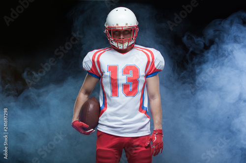 Front view portrait of american football player wearing helmet with ball against white smoke