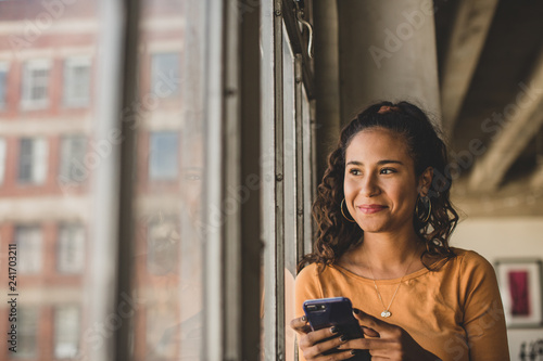 Smiling woman with smartphone looking through window