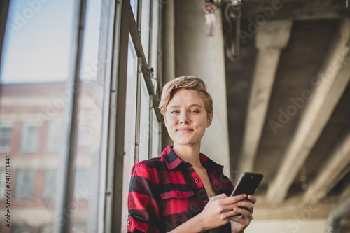 Portrait young female in loft apartment holding smartphone