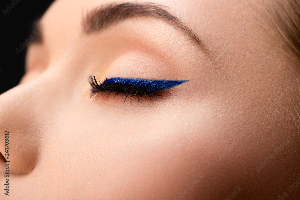 cropped view of closed female eye with blue eyeliner and perfect skin