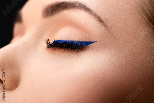 cropped view of closed female eye with blue eyeliner and perfect skin