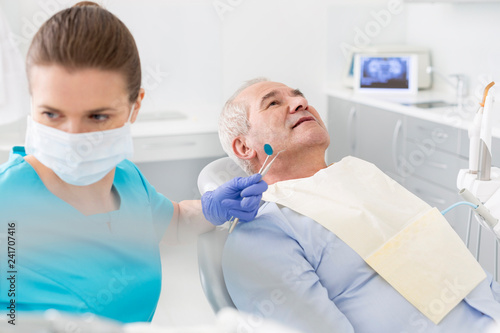 Canvas Print Mid adult dentist with equipment treating senior patient at clinic