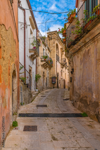 Fototapeta Naklejka Na Ścianę i Meble -  Italian narrow street with flower balconies in ancient baroque town Ragusa, Sicily, Italy