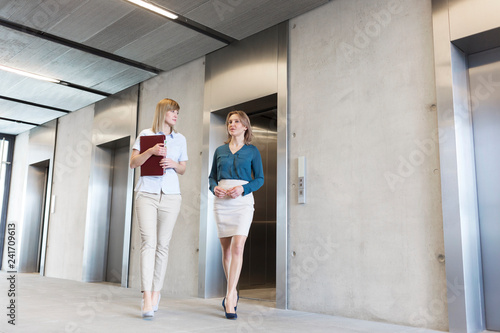 Businesswomen talking while walking out from elevator at office lobby photo