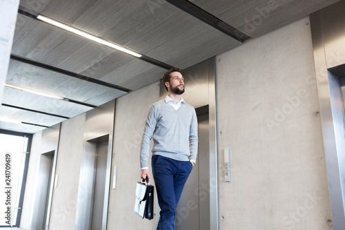 Confident businessman with briefcase walking in lobby at office photo