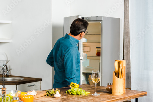 rear view of mature man looking into open fridge in kitchen