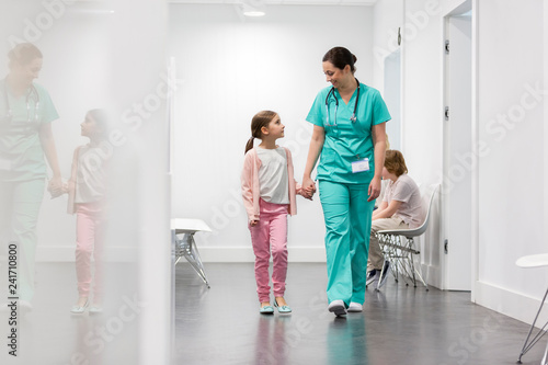 Smiling nurse walking with girl in corridor at hospital photo