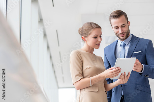 Fototapeta Confident young colleagues discussing over digital tablet at new office