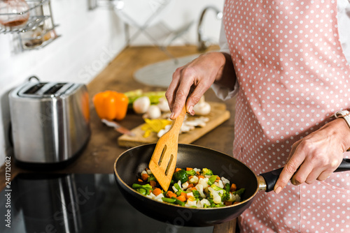 cropped image of mature woman frying vegetables in kitchen