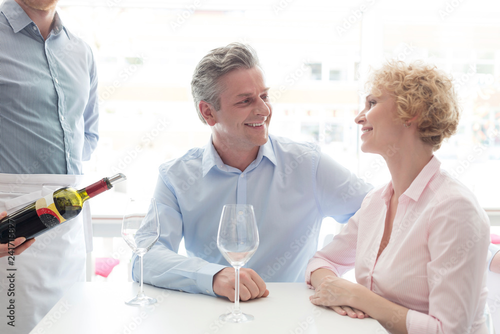 Obraz premium Midsection of young waiter serving wine to mature couple at restaurant