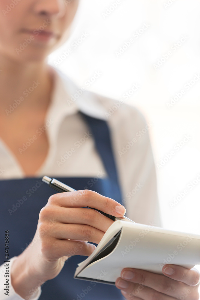 Midsection of young waitress writing on notepad at restaurant - obrazy, fototapety, plakaty 