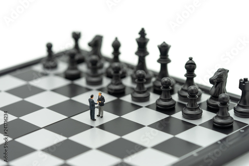 Miniature 2 people businessmen Shake hands on a chessboard with a chess piece on the back Negotiating in business. as background business concept and strategy concept with copy space.