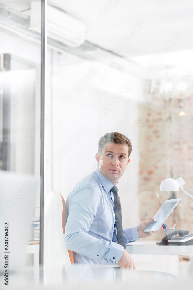Creative businessman holding digital tablet seen through glass wall