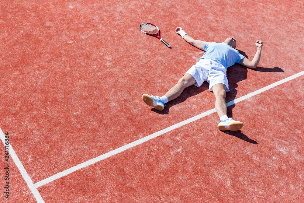 Full length of disappointed mature man lying by tennis racket on court during summer
