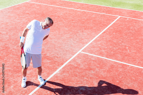 Full length of senior man standing with backache on red court during match on sunny day