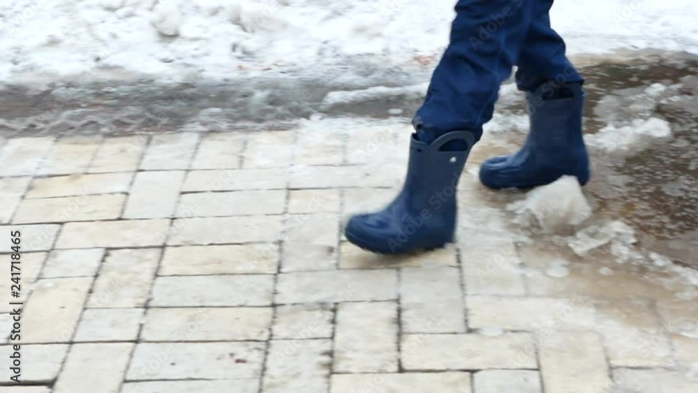 small kid in waterproof rubber boots walking from right to left on puddle of melted snow. closeup 4k outdoor video footage at winter season small kid in waterproof rubber boots walking from right to left on puddle of melted snow. closeup 4k outdoor video footage at winter season