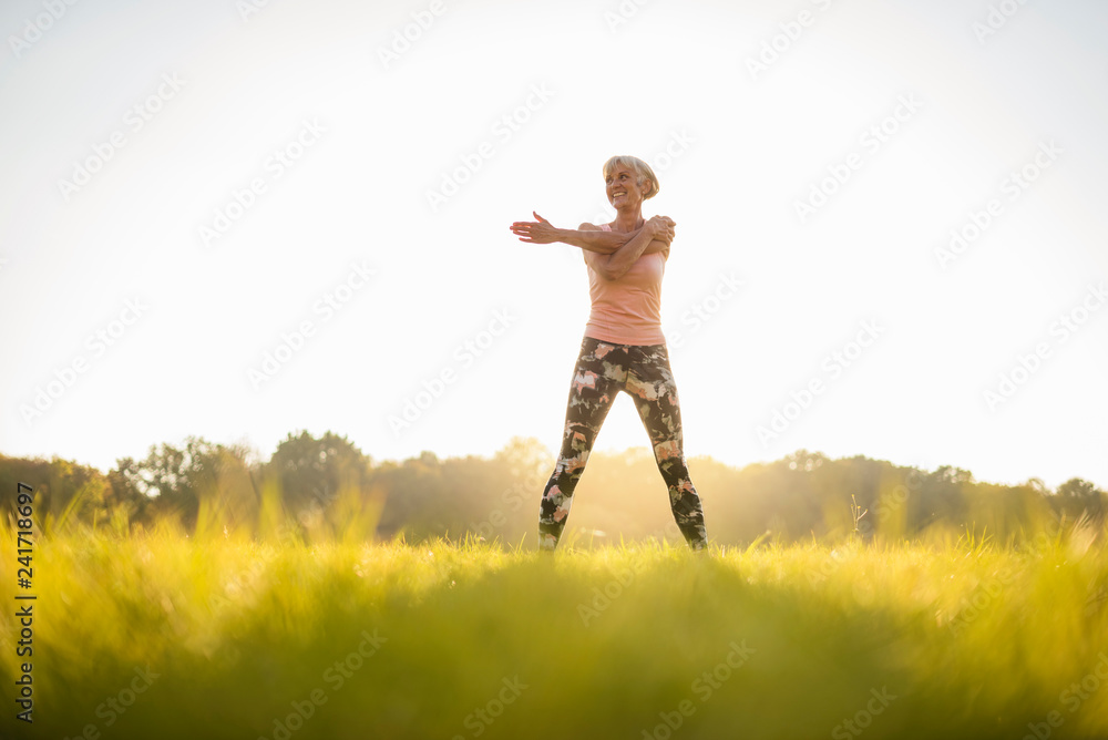 Senior woman stretching on rural meadow at sunset Senior woman stretching on rural meadow at sunset