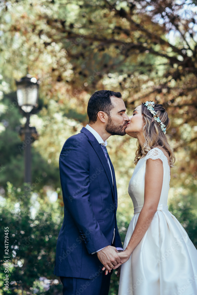 Happy bridal couple kissing in a park while holding hands Happy bridal couple kissing in a park while holding hands