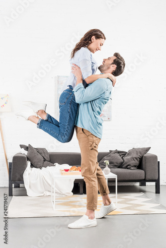 happy man in casual clothes holding woman in living room