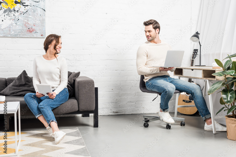 couple using digital devices and looking at each other in living room