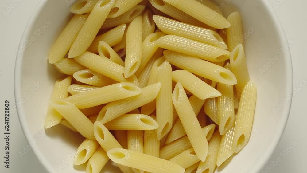 SLOW MOTION: Ribbed Penne pasta falling into a white plate - Top View