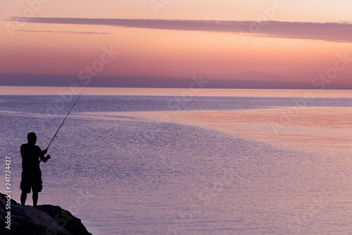 Silhouette of man with fishing spinning. Fishing on the lake at sunset. Lake Ontario. Rochester, USA