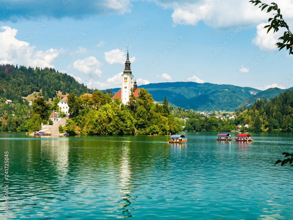 Lake Bled with its island, in Slovenia Europe, in summer, tourists on boats on a beautiful day with few clouds