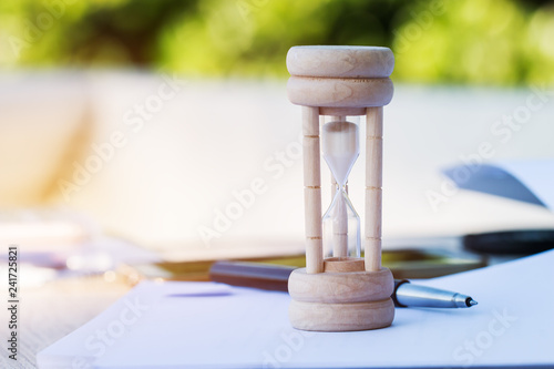 Wood hourglass / sandglass on paperwork, documents with pen. Invertible device with two connected glass bulbs containing sand takes an hour to pass from upper to  lower bulb. Concept business deadline photo