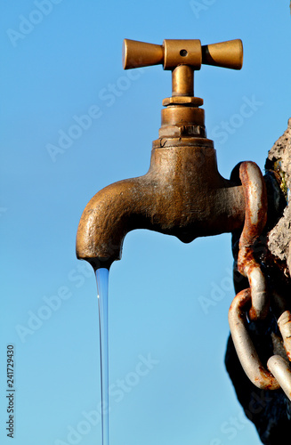 A brass faucet with clear clean water for the bypassers photo