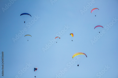 several paragliders on colorful parachutes in a clear blue sky