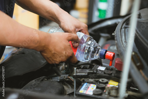 mechanic pouring distilled water to fill car battery in automobile repair service
