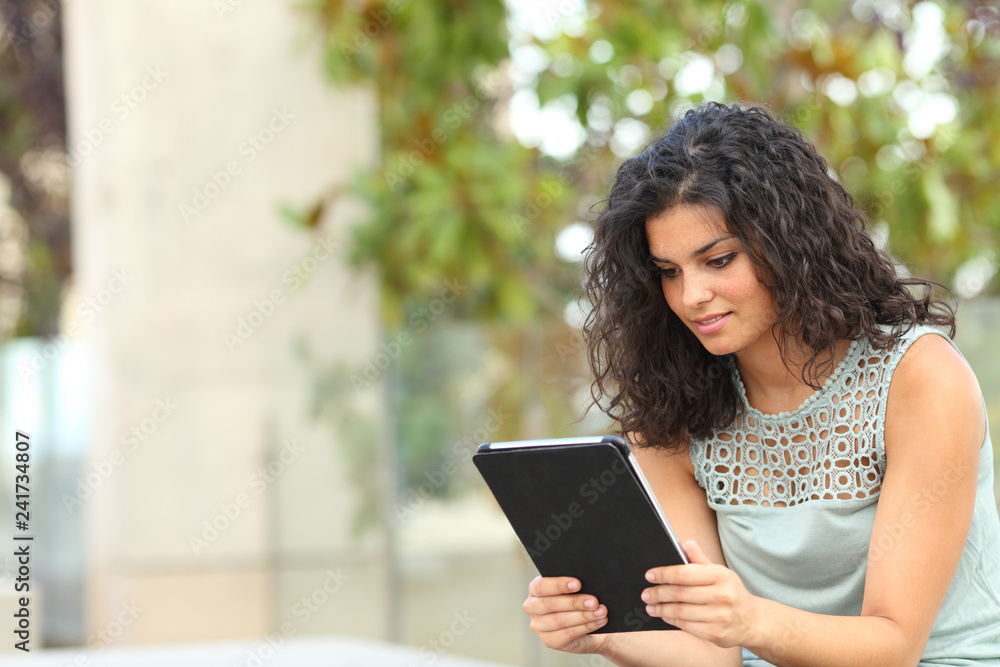 Woman using a tablet sitting in a bench in a park Woman using a tablet sitting in a bench in a park
