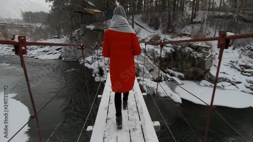 Woman in red coat goes on suspension bridge over the winter mountain river photo
