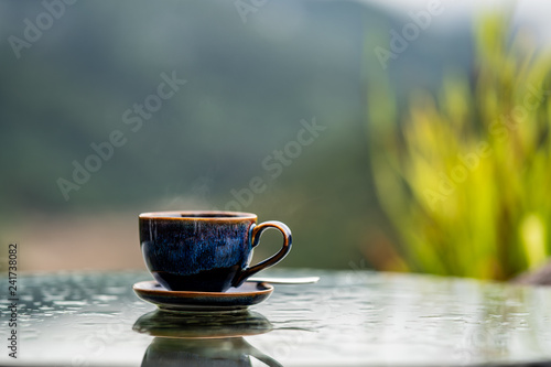 A cup of coffee is placed on the table with a tree background.