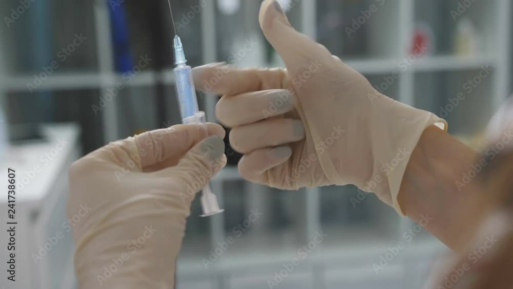 Close up of female doctor holding and squeezing syringe with medicine. Doctor putting a drip into the catheter lying patients close-up.Injection vaccine. Close up of female doctor holding and squeezing syringe with medicine. Doctor putting a drip into the catheter lying patients close-up.Injection vaccine.