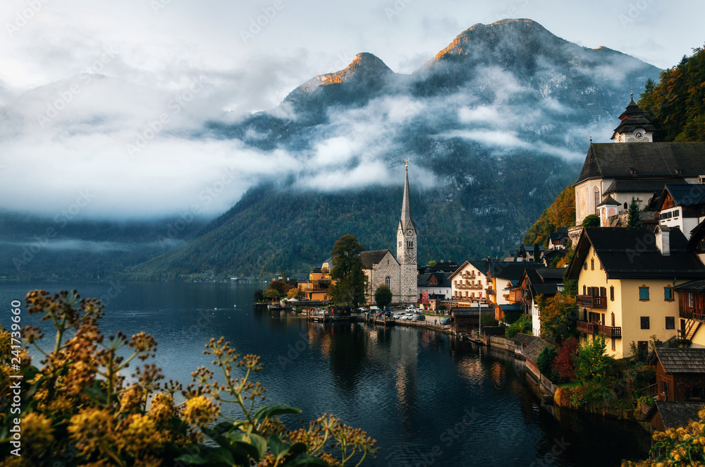 Scenic view of famous Hallstatt lakeside town reflecting in Hallstattersee lake in Austrian Alps in autumn morning light with bushes and flowers on the foreground, Salzkammergut region, Austria