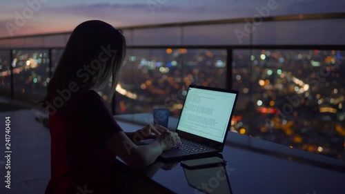 Young Businesswoman work on notebook computer on the balcony of a skyscraper on the background of a fascinating sunset and a view of the night city