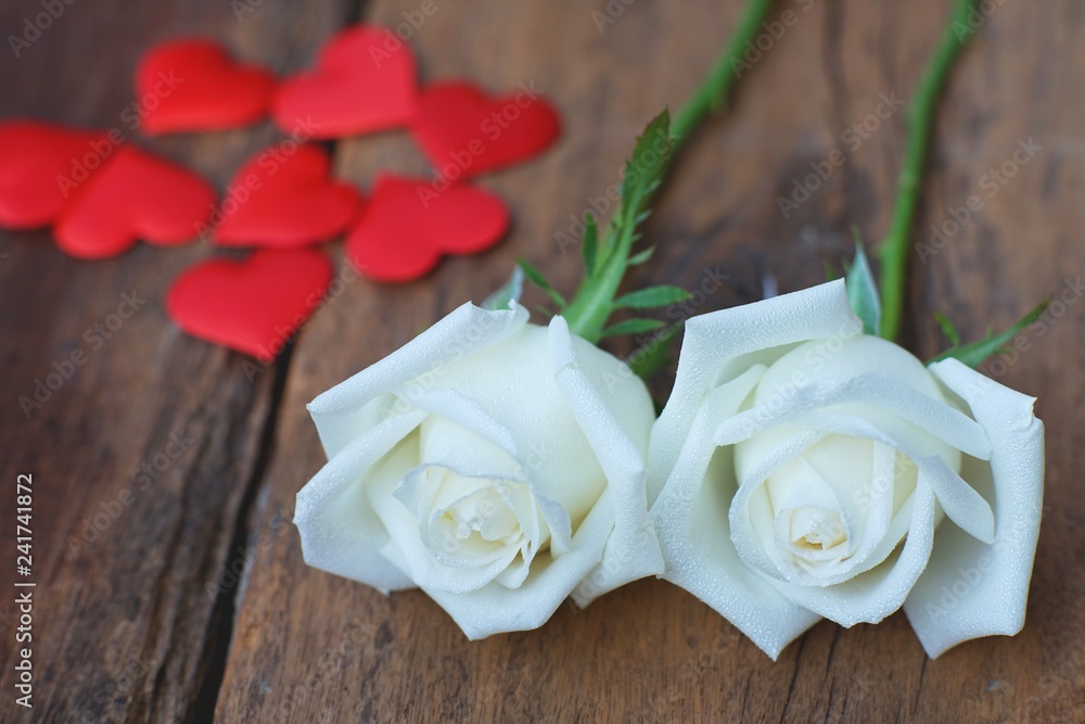 Beautiful white fresh moist rose flowers decorated with mini red heart figures on wood texture background, soft tone valentine flower concept Beautiful white fresh moist rose flowers decorated with mini red heart figures on wood texture background, soft tone valentine flower concept