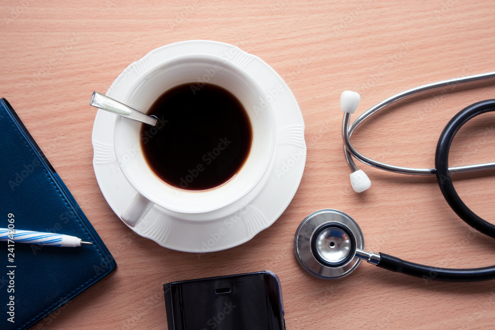 Top view of doctor desk with hot black coffee stethoscope and smartphone.