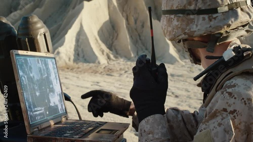 Military Operation in the Desert, Using Satellite or Drone Technology: Soldier with Laptop Monitors Movement of Armed Terrorist Vehicle, Uses Radio Communication to Call an Air Strike.