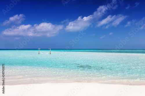 Tropischer Paradiesstrand mit Hängematte im türkisem Wasser und feinem Sand unter tiefblauem Himmel  © moofushi