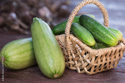 Fresh cucumbers in basket and zucchini on wooden background