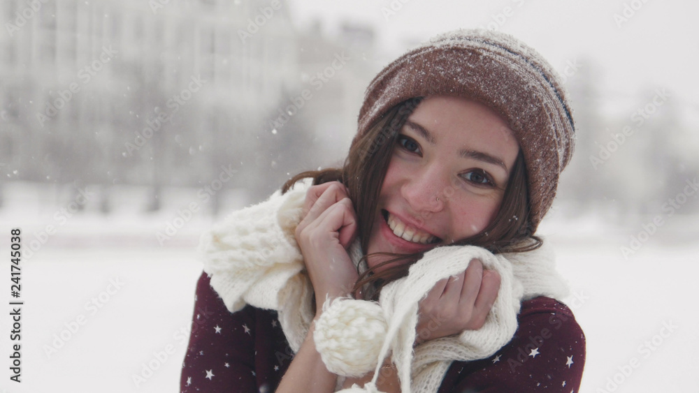 A young smiling woman standing in winter outside. Wearing white scarf and touching it with her hands A young smiling woman standing in winter outside. Wearing white scarf and touching it with her hands