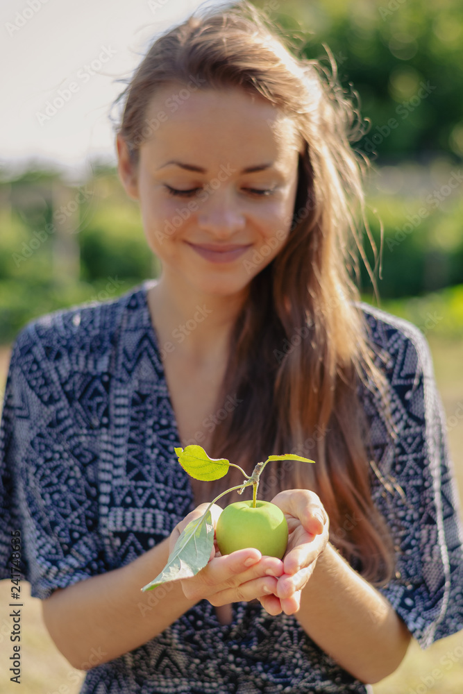 Summertime in garden. Young woman holding an apple in her hand. Summertime in garden. Young woman holding an apple in her hand.