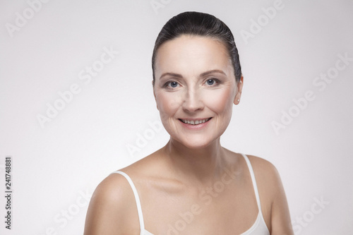 Closeup portrait of charming  pretty  attractive woman with perfect skin smiling after cream  balm  mask  lotion  isolated on grey background. Indoor  studio shot  copy space  advertisement concept