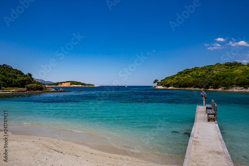 KSAMIL, ALBANIA - MAY 17, 2017: Female tourist on wooden sea pier with two benches made from pine tree planks enjoys the paradise views at the Albanian Riviera in bright sunny warm spring day.