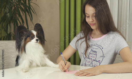 Girl teenager with dog Papillon guess on desires, writes desire to pieces of paper photo